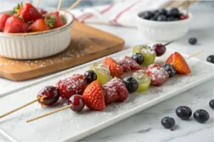 A close-up of glossy Tanghulu skewers with strawberries, grapes, and blueberries, coated in hardened sugar, placed on a white marble countertop in a bright white kitchen.